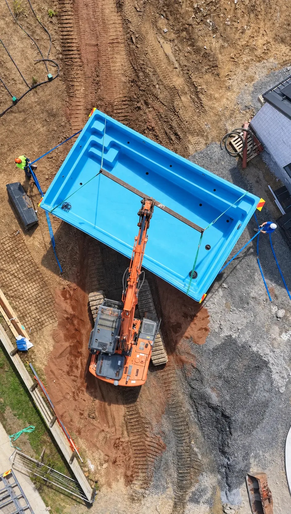 Aerial view of an excavator lifting the pool shell into position beside the house during construction at Coatesville Riverhead Highway