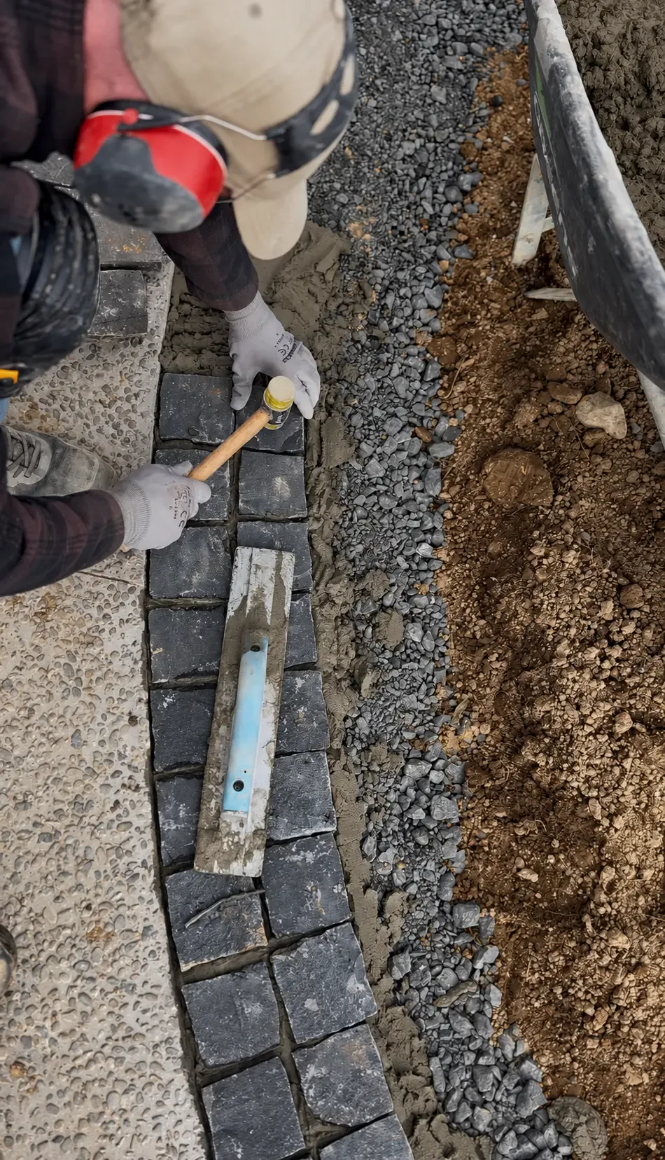 Landscape tradesman installing dark cobblestone edging beside exposed aggregate paving at Coatesville Riverhead Highway